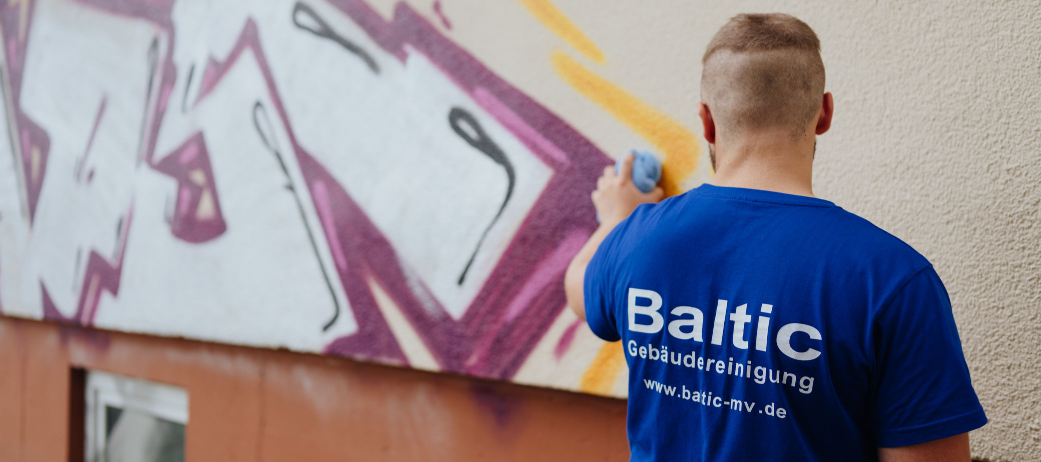Ein Mitarbeiter entfernt ein Graffiti an einer Wand.