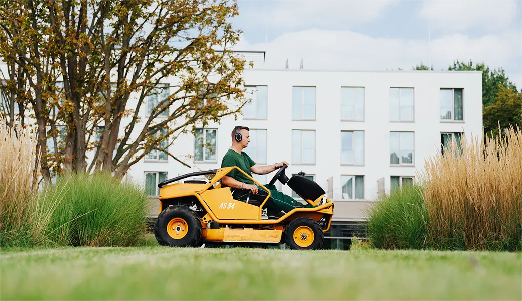 Ein Mitarbeiter fährt mit einem Rasentraktor über eine große Grasfläche.